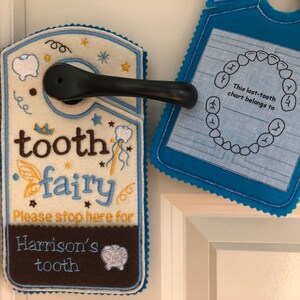 May include: A tooth fairy door hanger with a brown and white felt background. The hanger has a blue border and says "tooth fairy" in brown embroidery. It also says "Please stop here for Harrison's tooth".