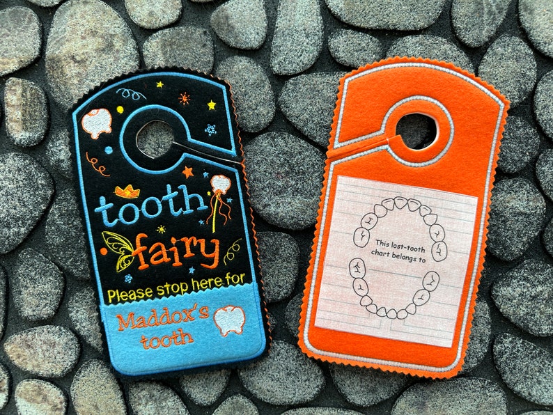 May include: Two tooth fairy door hangers. One is blue with black and yellow embroidery that says "tooth fairy" and "Please stop here for Maddox's tooth". The other is orange with white embroidery that says "This lost-tooth chart belongs to".