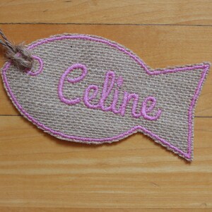 May include: A burlap fish-shaped tag with a pink embroidered name "Celine" on it.