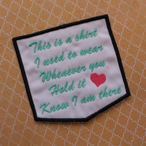 May include: White fabric patch with black stitching around the edges. The patch has green embroidered text that reads "This is a shirt I used to wear Whenever you Hold it Know I am there". A pink heart is embroidered above the last line of text.