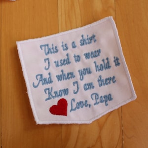 May include: White fabric patch with blue embroidered text that reads "This is a shirt I used to wear And when you hold it Know I am there Love, Papa" with a red embroidered heart.