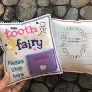 May include: A white felt tooth fairy pillow with a purple pocket that says "Reese" and the text "tooth fairy" embroidered on it. The pillow also has the text "Please stop here" embroidered on it. A white felt pillow with a tooth chart and the text "This lost-tooth chart belongs to" is next to it.