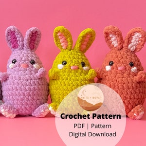 May include: Three crocheted bunny amigurumi toys in purple, yellow, and orange. The bunnies are sitting on a pink background. The image includes the text "Crochet Pattern PDF | Pattern Digital Download".