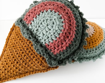 May include: A crocheted ice cream cone toy with a multi-colored scoop. The cone is brown and the scoop is green, pink, and light blue.