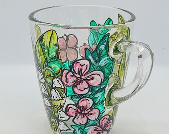 May include: A clear glass mug with a painted design of pink and white flowers and green leaves.