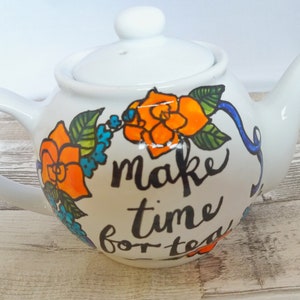 Pu&ograve; includere: Teiera in ceramica bianca con un design floreale e il testo "make time for tea".