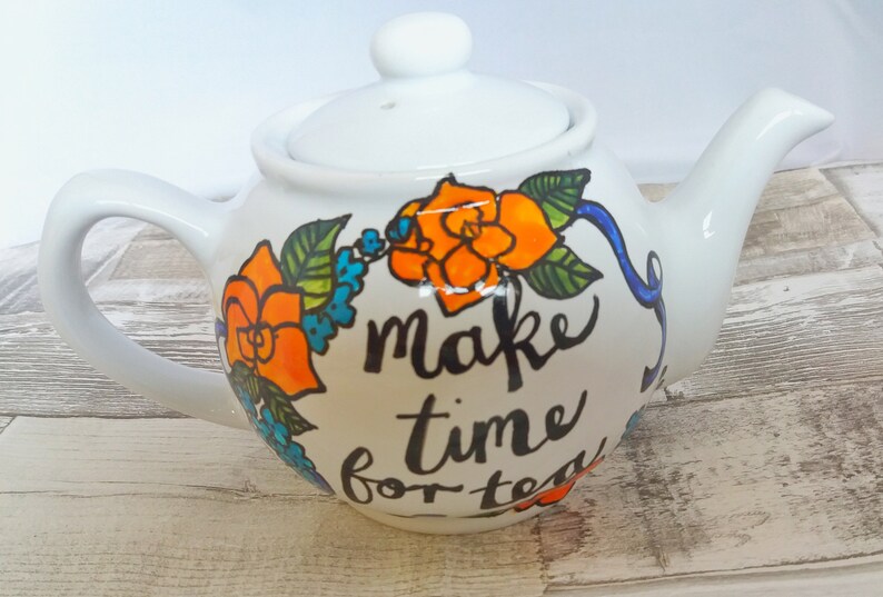 Pu&ograve; includere: Teiera in ceramica bianca con un design floreale e il testo "make time for tea".