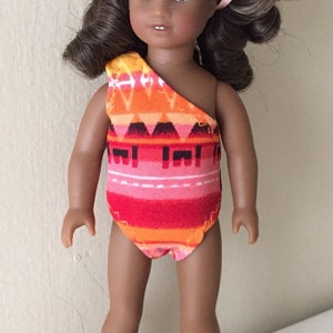 May include: A brown-skinned doll with long brown hair wearing a red, orange, and black patterned swimsuit.