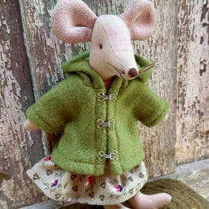 May include: A handmade fabric mouse doll with large pink ears, wearing a green hooded jacket with silver clasps and a floral print skirt. The doll is posed on a wooden surface.