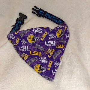 May include: Purple and gold dog bandana with a repeating pattern of LSU Tigers logos and the words "LSU Tigers". The bandana has a blue and black adjustable collar.