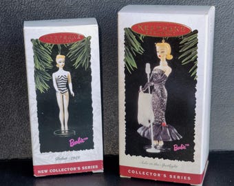 Könnte beinhalten: Zwei Barbie-Puppenboxen. Eine Box zeigt eine Barbie in einem schwarz-weiß gestreiften Badeanzug mit der Aufschrift "Debut - 1959". Die andere Box zeigt eine Barbie in einem glitzernden Kleid mit der Aufschrift "Solo in the Spotlight". Beide Boxen gehören zur Collector's Series.