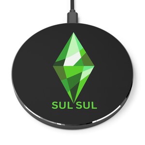 Könnte beinhalten: Schwarzes kabelloses Ladegerät mit silberner Umrandung. Es zeigt eine grüne rautenförmige Grafik mit verschiedenen Grüntönen und dem grünen Text "SUL SUL". Ein schwarzes Kabel erstreckt sich von oben.
