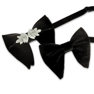 May include: Two black velvet bow ties. One bow tie has a silver floral embellishment. The other bow tie is plain. Both bow ties have adjustable black straps. The bow ties are likely for formal wear.