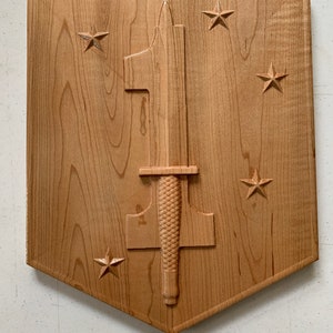 May include: A wooden plaque with a carved image of a dagger and five stars. The plaque is shaped like a shield.