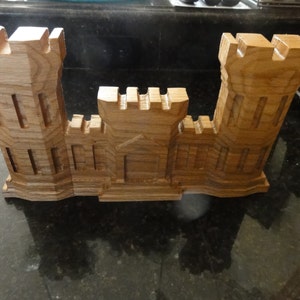 May include: A wooden model of a castle with two towers and a central section. The model is made of light brown wood and has a detailed design.
