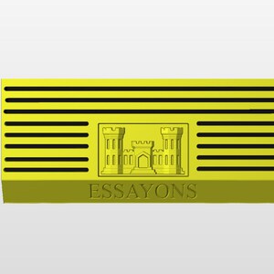 May include: A yellow rectangular emblem with horizontal black lines and a central embossed design of a castle. The word "ESSAYONS" is embossed at the bottom. The emblem has a three-dimensional appearance.