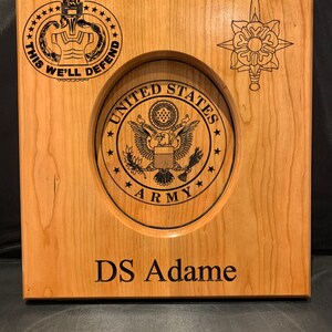 May include: A wooden plaque featuring a United States Army seal, a military insignia, and the text "This We'll Defend" and "DS Adame".