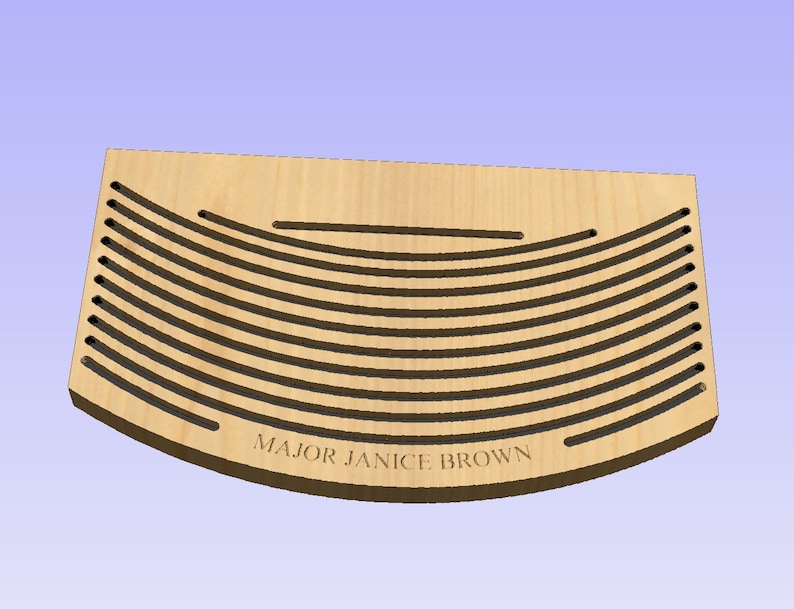 Puede incluir: Una placa de madera con forma curva y una serie de l&iacute;neas paralelas cortadas en la superficie. La placa tiene el texto "MAJOR JANICE BROWN" grabado en el borde inferior.