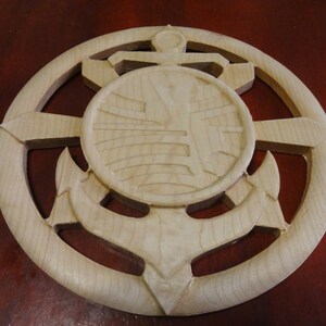 May include: A wooden wall decor featuring a carved anchor with a circular design in the center. The anchor is surrounded by a decorative frame.