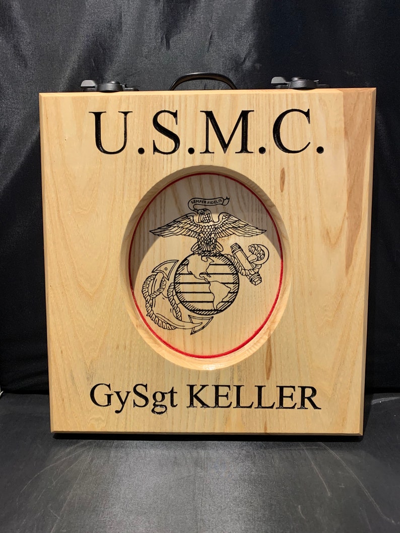 May include: A wooden plaque with the words "U.S.M.C." and "GySgt KELLER" engraved on it. The plaque features a carved image of the Marine Corps emblem, a globe with an eagle perched on top and an anchor below, surrounded by a red circle.