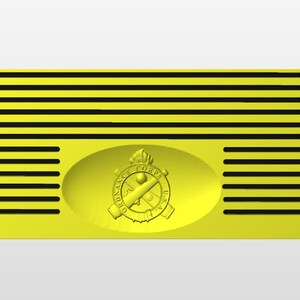 Op de afbeelding: Een gele metalen plaquette met een zwart-wit ontwerp van gekruiste kanonnen en een brandende lont. De tekst "ORDNANCE CORPS U.S. ARMY" is rond het ontwerp gegraveerd. De plaquette heeft een reeks horizontale zwarte lijnen.