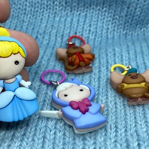 May include: Four colorful charms featuring characters from a fairy tale. One charm depicts a princess in a blue dress with blonde hair. Other charms include two mice and a character in a blue coat.