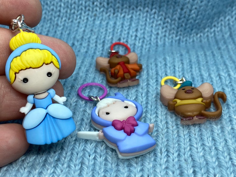 May include: Four colorful charms featuring characters from a fairy tale. One charm depicts a princess in a blue dress with blonde hair. Other charms include two mice and a character in a blue coat.