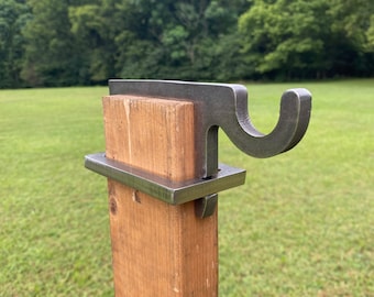 May include: A metal hook attached to a wooden post. The hook is made of metal and has a simple design. The post is made of wood and is painted brown.