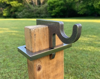 May include: A metal hook mounted on a wooden post. The hook is a simple, curved design with a rustic finish.
