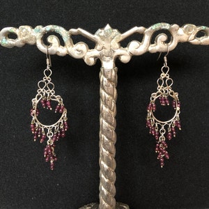 May include: A pair of silver dangle earrings with a circular design and dangling garnet beads.