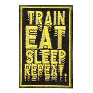 May include: A rectangular embroidered patch with a black background and a yellow border. The patch features the yellow embroidered text TRAIN EAT SLEEP REPEAT. The letters have a layered, three-dimensional effect with a slight shadow design.