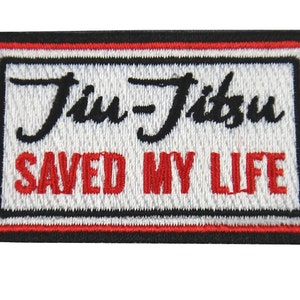 May include: A rectangular embroidered patch with a white background and a black, white, and red border. The text Jiu-Jitsu is stitched in black cursive, and the text SAVED MY LIFE is stitched in red block letters below it.