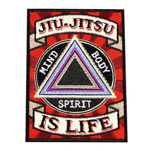 May include: A rectangular embroidered patch featuring a red sunburst background. It displays the text JIU-JITSU on a top banner and IS LIFE on a bottom banner. A central black triangle is surrounded by concentric borders with the words MIND, BODY, SPIRIT.