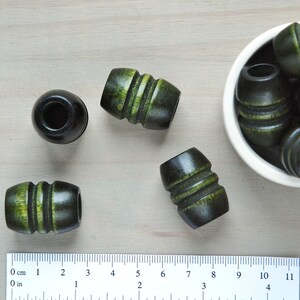 May include: A collection of dark green wooden beads with light green stripes. Some beads are in a white bowl, while others are on a wooden surface next to a ruler.
