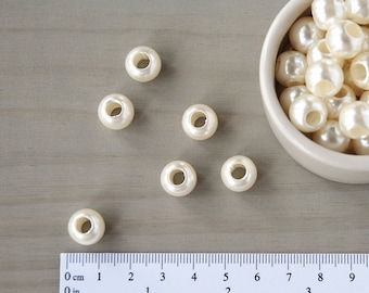 Könnte beinhalten: Eine Schüssel mit weißen Plastikperlen, die jeweils ein Loch in der Mitte haben. Außerdem liegen mehrere Perlen auf einer Holzoberfläche neben einem Lineal.