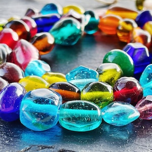 May include: A strand of colorful glass beads in various shapes and sizes. The beads are a mix of transparent and opaque, with colors including blue, red, orange, green, and yellow. The beads are strung together on a thin, off-white cord.