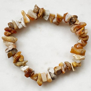 Pode incluir: Um bracelete feito de pequenas pedras irregulares de cor castanho, branco e amarelo.