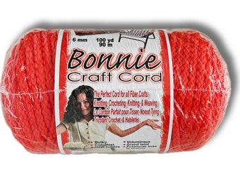 Op de afbeelding: Een rol rode Bonnie Craft Cord, 6 mm dik, 100 yards (90 meter) lang. Het etiket zegt "The Perfect Cord for all Fiber Crafts: Knotting, Crocheting, Knitting, & Weaving. Le Cordon Parfait pour Tisser, Noeud Tying, Tricotant Crochet, & Habiletés..." Het zegt ook "Bulky Colorfast Heat fusible" en "Volumineux Grand teint Fusionner avec la chaleur."