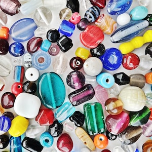 Puede incluir: Una gran colección de cuentas de vidrio de colores en varias formas y tamaños. Las cuentas son una mezcla de colores opacos y transparentes, incluyendo rojo, azul, verde, amarillo y blanco.