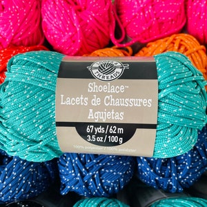 Puede incluir: Un cordón de zapato azul turquesa con puntos blancos, etiquetado "Shoelace™ Lacets de Chaussures Agujetas 67 yds/62 m 3.5 oz/100 g 100% polyester/100% poliéster".