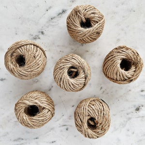 May include: Six balls of natural twine rope, each wound into a ball shape, on a white marble surface.