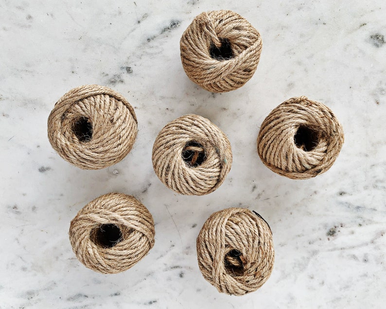 May include: Six balls of natural twine rope, each wound into a ball shape, on a white marble surface.