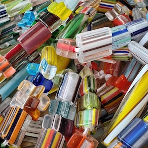 May include: A collection of rectangular glass beads featuring various colour combinations, including stripes of yellow, blue, red, green, and white. The beads have a smooth, translucent finish and are strung together in a dense, overlapping arrangement.