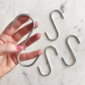May include: Five silver S-shaped hooks. One hook is being held in a hand.