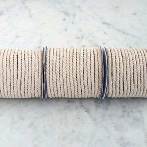 May include: Three spools of natural colored cotton rope, each wound around a cardboard core.