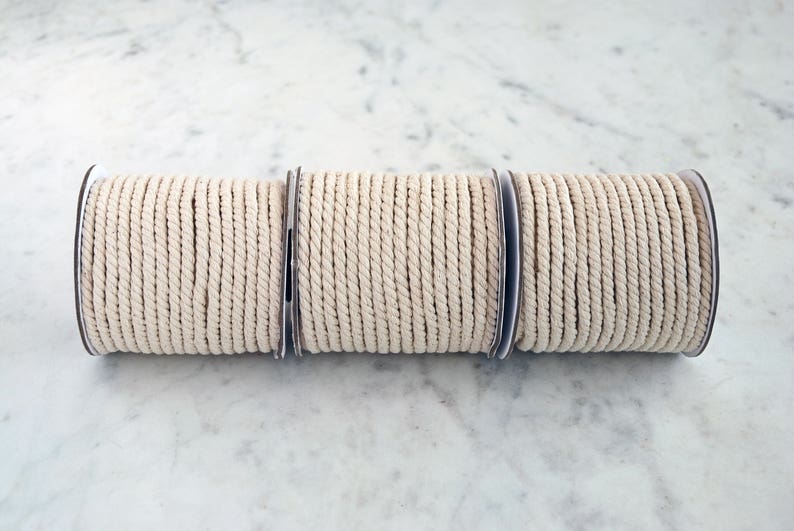 May include: Three spools of natural colored cotton rope, each wound around a cardboard core.