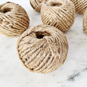 May include: Five balls of natural twine, each wound into a round shape. The twine is a light brown color and has a rough texture.