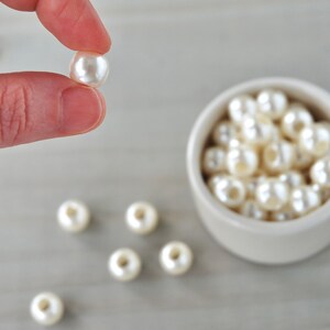 May include: A bowl filled with white pearl beads, with one pearl bead held between two fingers.