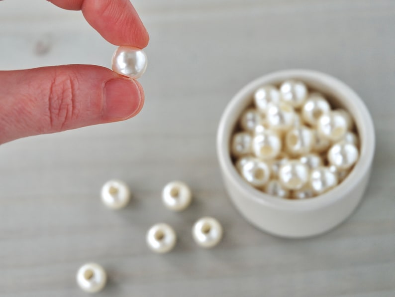 May include: A bowl filled with white pearl beads, with one pearl bead held between two fingers.