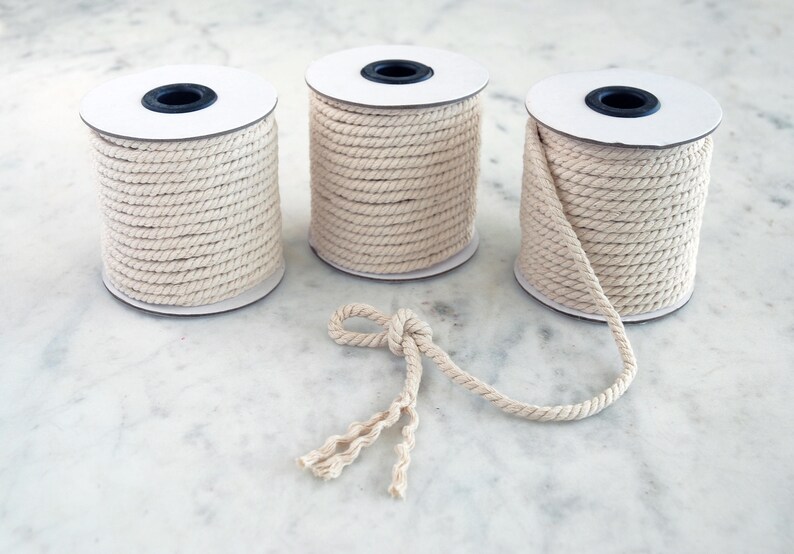 May include: Three spools of natural cotton rope, each wound on a white cardboard spool. A length of rope is pulled out and tied in a knot.